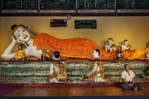 YANGON, MYANMAR, JANUARY 3, 2014: Man meditating near statue of Recumbent Buddha in Shwedagon Paya