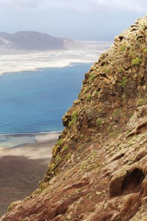 Rocky cliffs overlook the blue sea, under a wide sky, La Graciosa in the distance in the