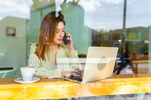 Millennial woman working remotely from a cafe while conversing on a smartphone, connecting with