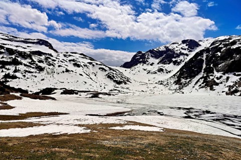 Ice floes drift in the half-frozen upper Murgsee, in the foreground, white flowering spring