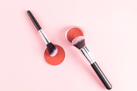 A stylish arrangement of makeup brushes with bristles dipped in a warm-hued compact blush, set