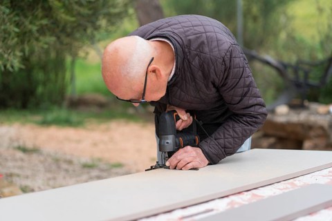 Senior man meticulously using a jigsaw on a piece of wood in an outdoor setting, focusing intently