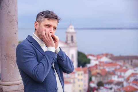 Man musician in a blue blazer and white sweater playing blues on a harmonica with eyes closed,