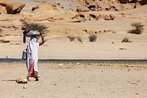 A single person carries loads in the remoteness of the desert, woman washing clothes in the Sahara