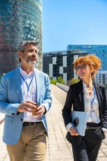 Two business professionals stroll through the city, chatting over coffee and a laptop, portraying
