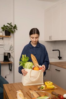 A teenage girl holds a grocery bag filled with fresh produce, including lettuce, celery, and bread,