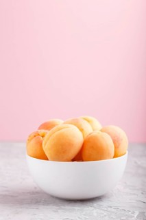 Fresh orange apricots in white bowl on gray and pink pastel background. side view, copy space,