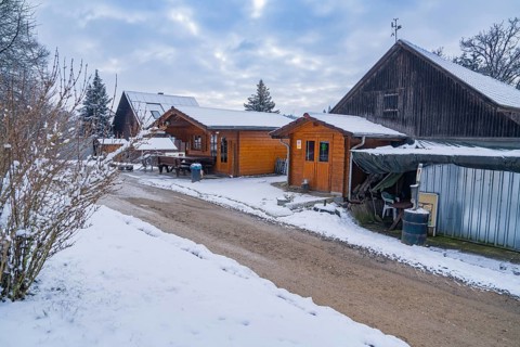 Snow-covered wooden houses along a rural path under a cloudy winter sky, farm shop of Haselstaller
