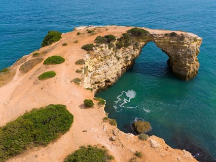 Natural rock arch by the sea, surrounded by water and some vegetation, aerial view, Arco de