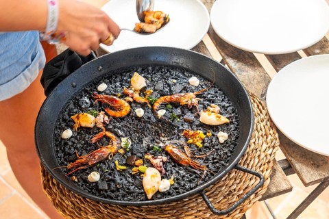 Chef serving a traditional black rice paella with shrimps and seafood, using a spoon, directly from