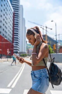 Young woman with headphones and phone feeling happy while navigating a bright summer day street,
