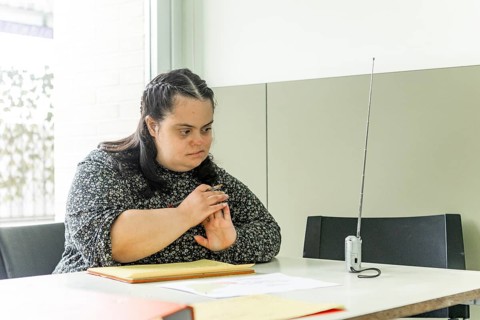 A woman is sitting at a table with documents in a mental health residence, looking contemplative,