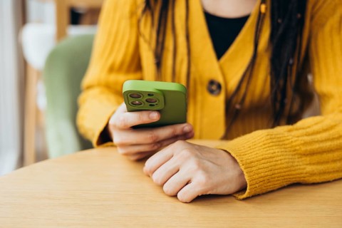 A person in a cozy yellow sweater holds a green smartphone, engaging with its screen The casual
