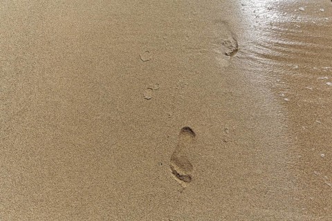 Gentle wave on the shore blurs footprint in the sand, Simos beach, text free space, symbolic photo,