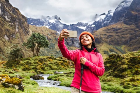 Ecuadorian woman wearing a pink jacket takes a selfie with a stunning backdrop of El Altar volcano,