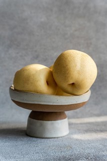 Three Chinese white pears are elegantly arranged on a rustic ceramic plate against a soft gray