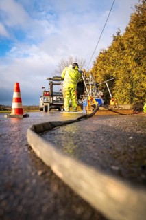 Worker prepares cable spool installation next to an emergency vehicle and barrier cones, fibre
