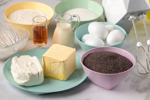 Baking ingredients such as poppy seeds, eggs, butter, milk and rum on a work surface