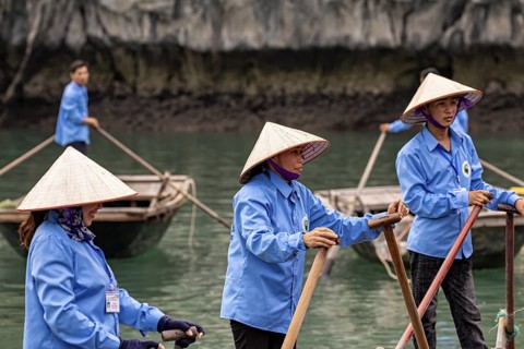 Several rowers in blue rowing on the river, surrounded by green nature and rocks, rowing boats for