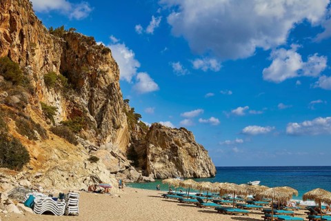 A picturesque beach with turquoise blue water and rocks in the background under a clear blue sky,