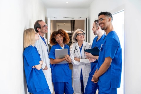 Happy multiethnic medical team of doctors and nurses in scrubs and lab coats standing in a clinic