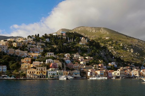 Colourful houses built on a green hill on the coast under a slightly cloudy sky, Symi Town, Symi,