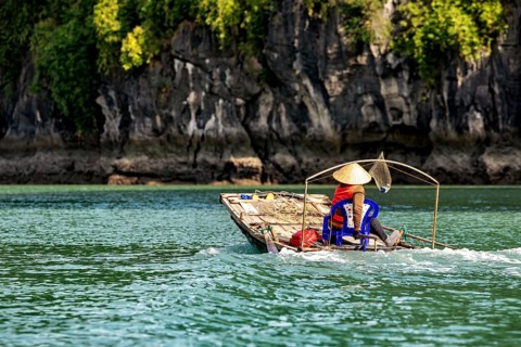 A dugout canoe with a seated person glides silently through clear, green water against a forested