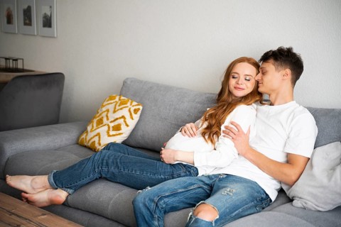 A young couple, joyfully expecting a baby, relaxes on a comfortable sofa in a cozy living room.
