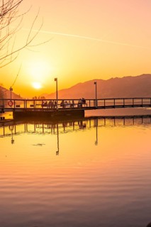Jetty at sunset with silhouettes of people at the lake, peaceful and warm atmosphere, Großer
