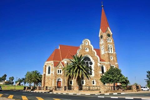 A historic church with a red roof against a clear blue sky, surrounded by trees, The historic