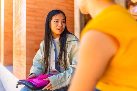 Chinese girl talking with a female caucasian friend sitting in the university campus