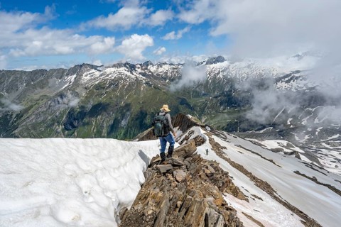 Mountaineer on a rocky ridge with snow, descent from the summit of Schönbichler Horn, view of