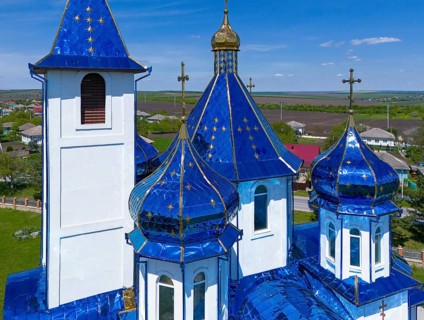 Close-up of blue church towers and roof with golden cross against rural backdrop, aerial view,
