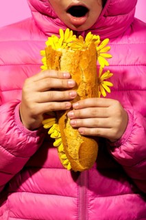 A striking image of a girl in a pink jacket holding a baguette interwoven with yellow flowers