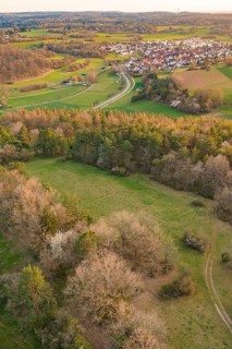 Broad landscape with meadows and forest surrounding a village and a curved road, e-bike tour, old