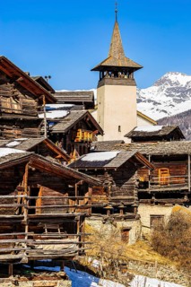 Snow-covered roofs of old farmhouses and barn storage, in the back the church tower of the Saint
