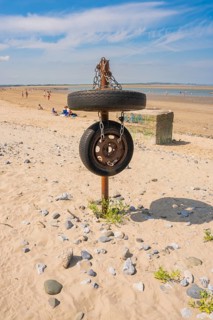 Old tires on posts as a sculptural element on sandy beach, blue sky, low tide, Howth beach, Ireland