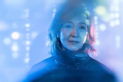 An elderly Asian woman is seen immersed in a futuristic digital environment, symbolizing the blend