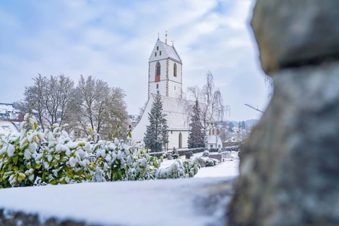 Winter view of a snow-covered church with trees and cemetery under a blue sky, Aidlingen, district