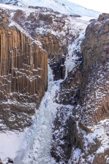 Hengifoss waterfall frozen in the cold Icelandic winter, detail of the volcanic cliffs