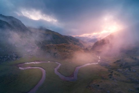 A beautiful sunrise over a misty valley, highlighting a winding river in the Pyrenees. The soft