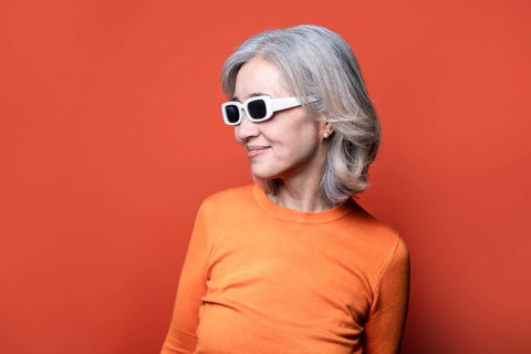 Asian Chinese senior woman with grey hair wearing trendy white sunglasses and an orange sweater.