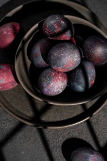 Top view of a ceramic bowl filled with dark, galaxy themed Easter eggs against dark background