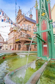 Historic town square with green fountain and colourful pennants in front of an old building,