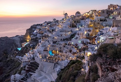 Cliff-side houses, villas and windmill in the village of Ia seen from Oia Castle at dusk,