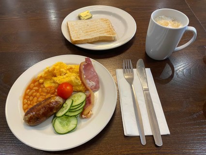 English breakfast on plate with scrambled eggs, baked beans, bacon, sausage, pickles, tomatoes,