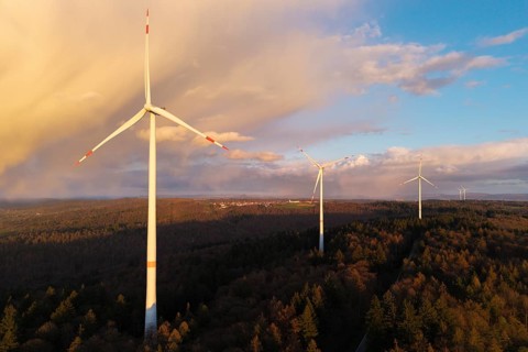 Three wind turbines looking up in a wooded landscape against a blue sky, wind turbine, near