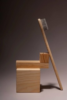 A bamboo toothbrush stands against a wooden block backdrop on a soft brown surface. The natural