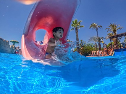Happy child exiting a pink waterslide and splashing into a blue swimming pool at a water park,