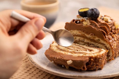 Sweet loaf with cream and carmel with hand, cup of coffee, on brown concrete background with linen